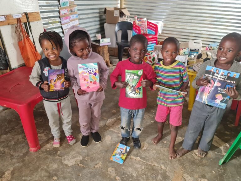 Five smiling children at Mercy Say Yes Preschool in Namibia hold up donated storybooks in their classroom