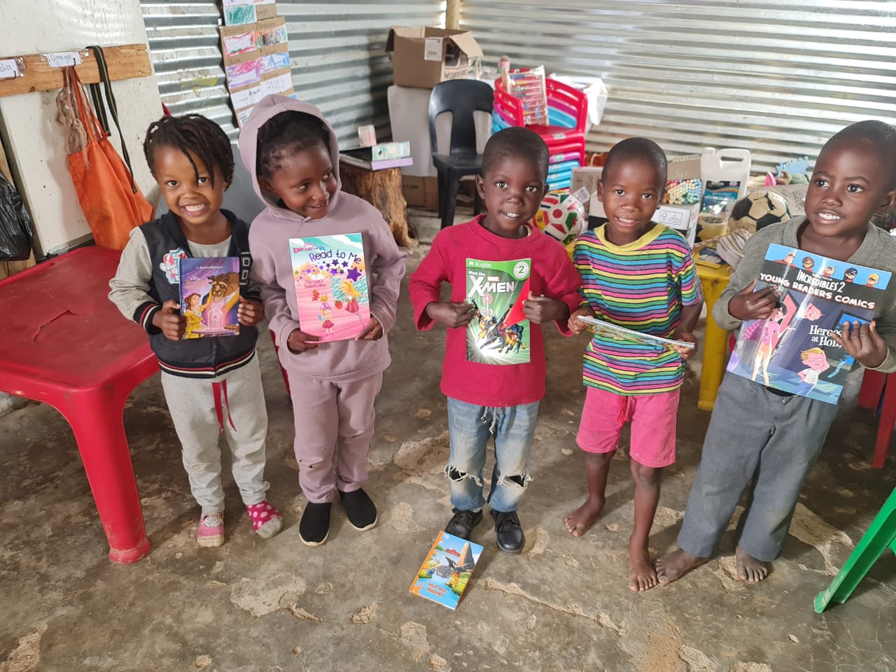 Five smiling children at Mercy Say Yes Preschool in Namibia hold up donated storybooks in their classroom